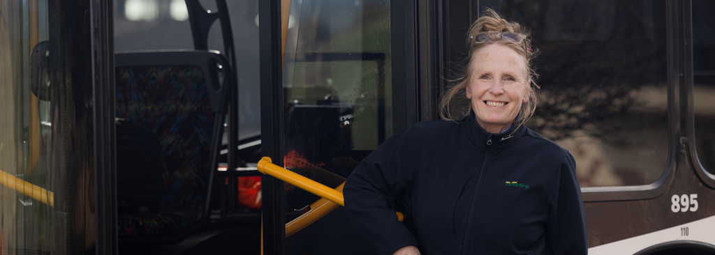 Female bus driver smiling outside of bus